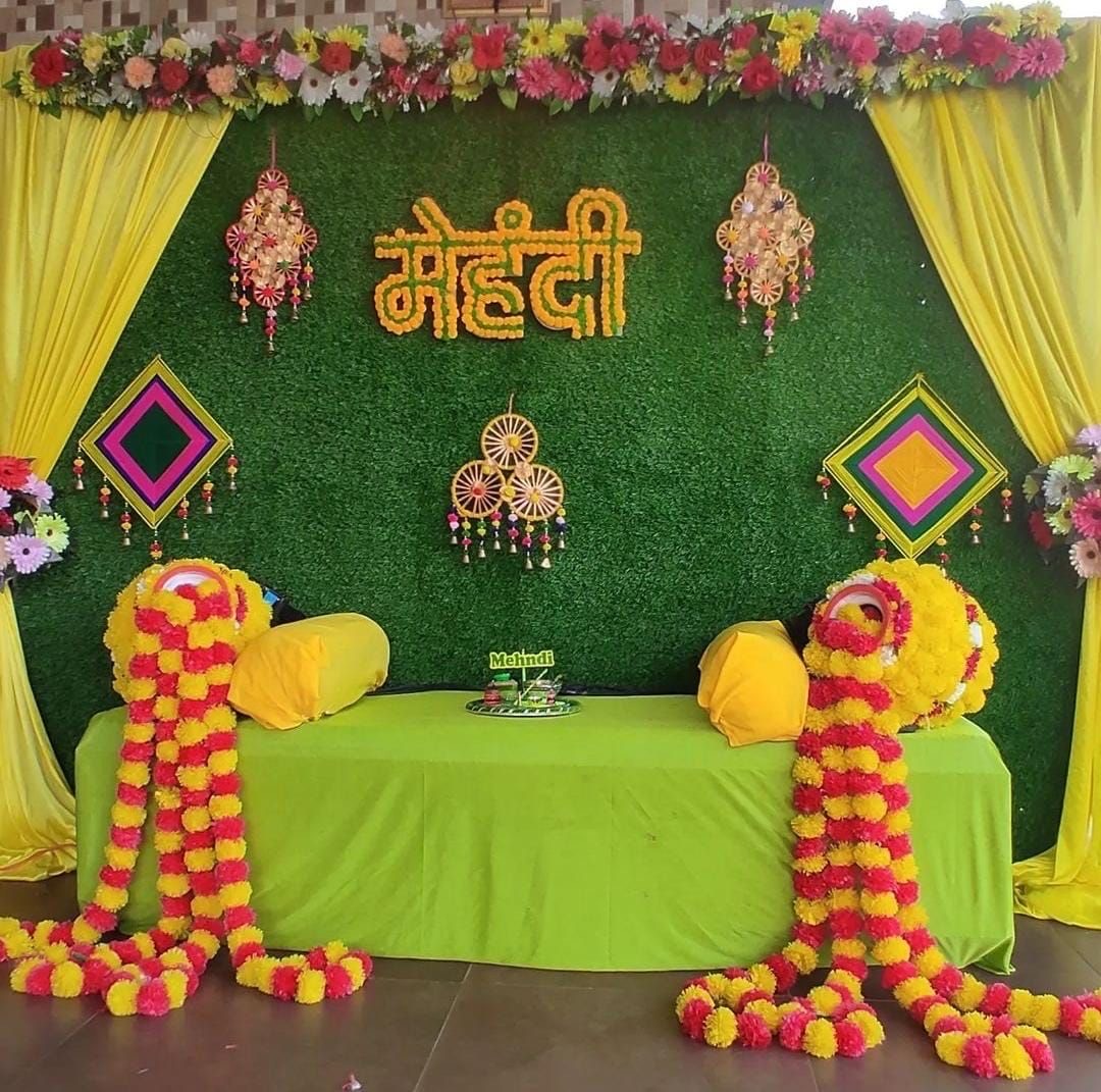Mehndi decoration in Hyderabad with a green grass wall, marigold lettering, yellow drapes and low seating with bolster cushions