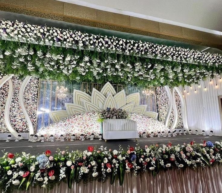 Reception decoration in Hyderabad with a white and green hanging floral ceiling, lotus backdrop and decorated couple seating